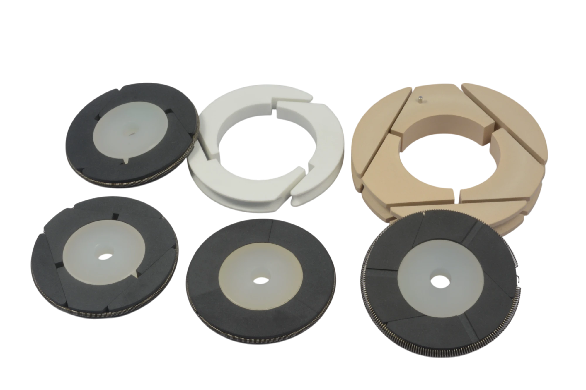 Assorted circular plastic components and reels, including dark gray spools, a white ring piece, and beige segmented rings, arranged on a black background.