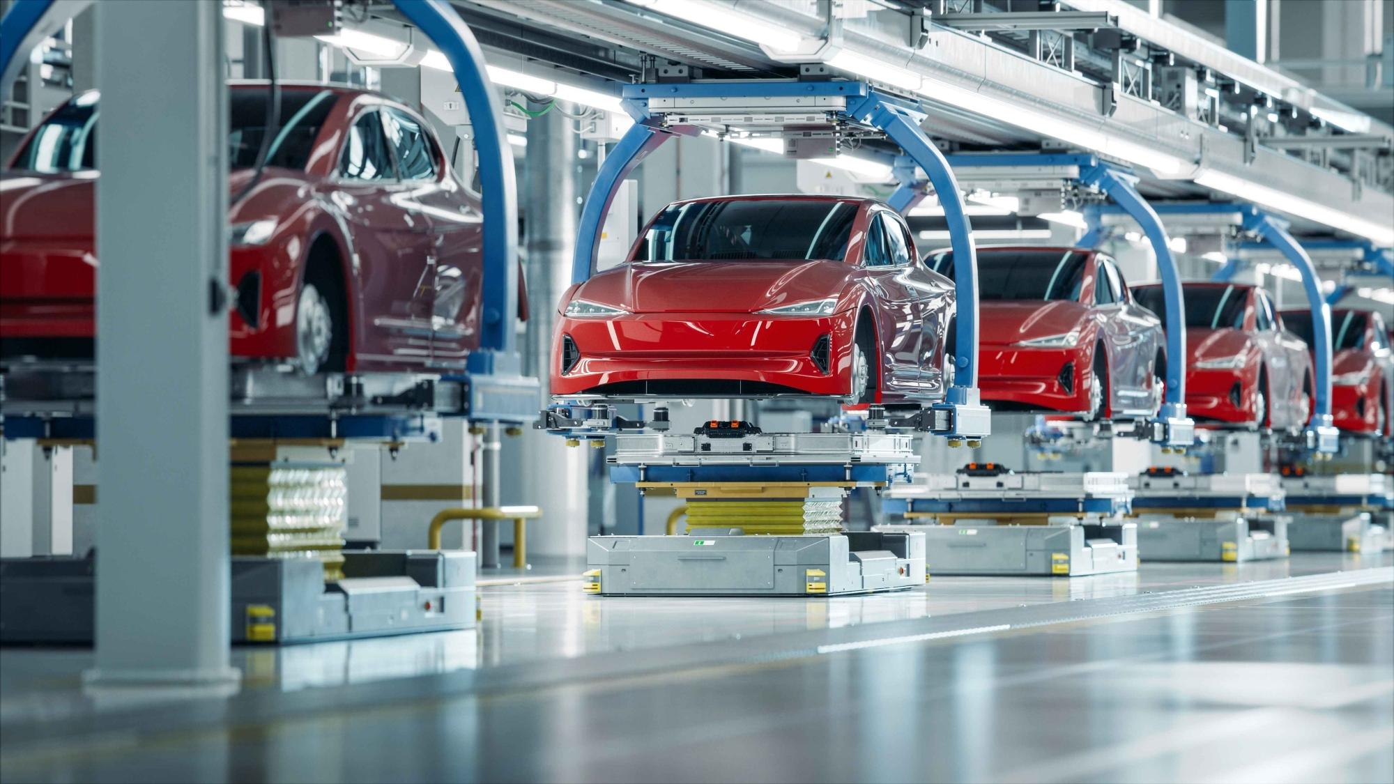 Red cars on an automated automotive assembly line under overhead robotic equipment in a modern factory setting