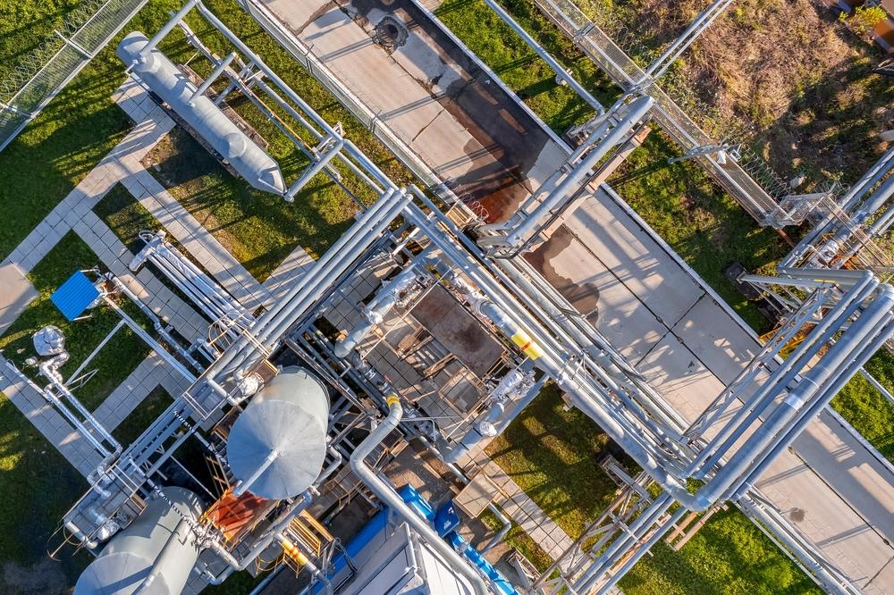 Aerial view of a complex network of silver steel pipes, tanks, and walkways at an industrial facility with surrounding greenery.