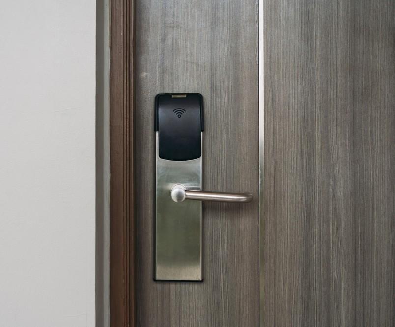 Electronic smart door lock mounted on a wooden door, with a silver lever handle. It has a black top unit with a wifi icon on it.