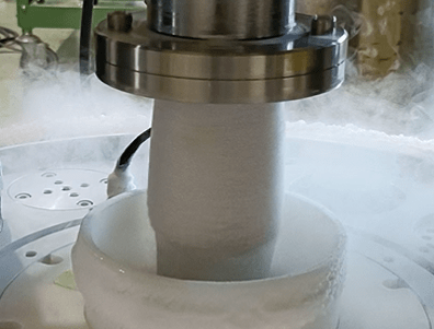 Close-up of a vertical spindle entering a frosty white chamber with mist, in an industrial lab setup.
